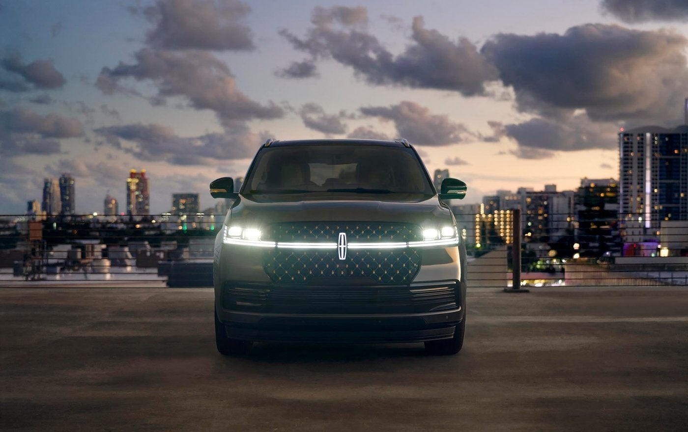 Front of a Lincoln Navigator with its slim headlights and light bar glowing at dusk