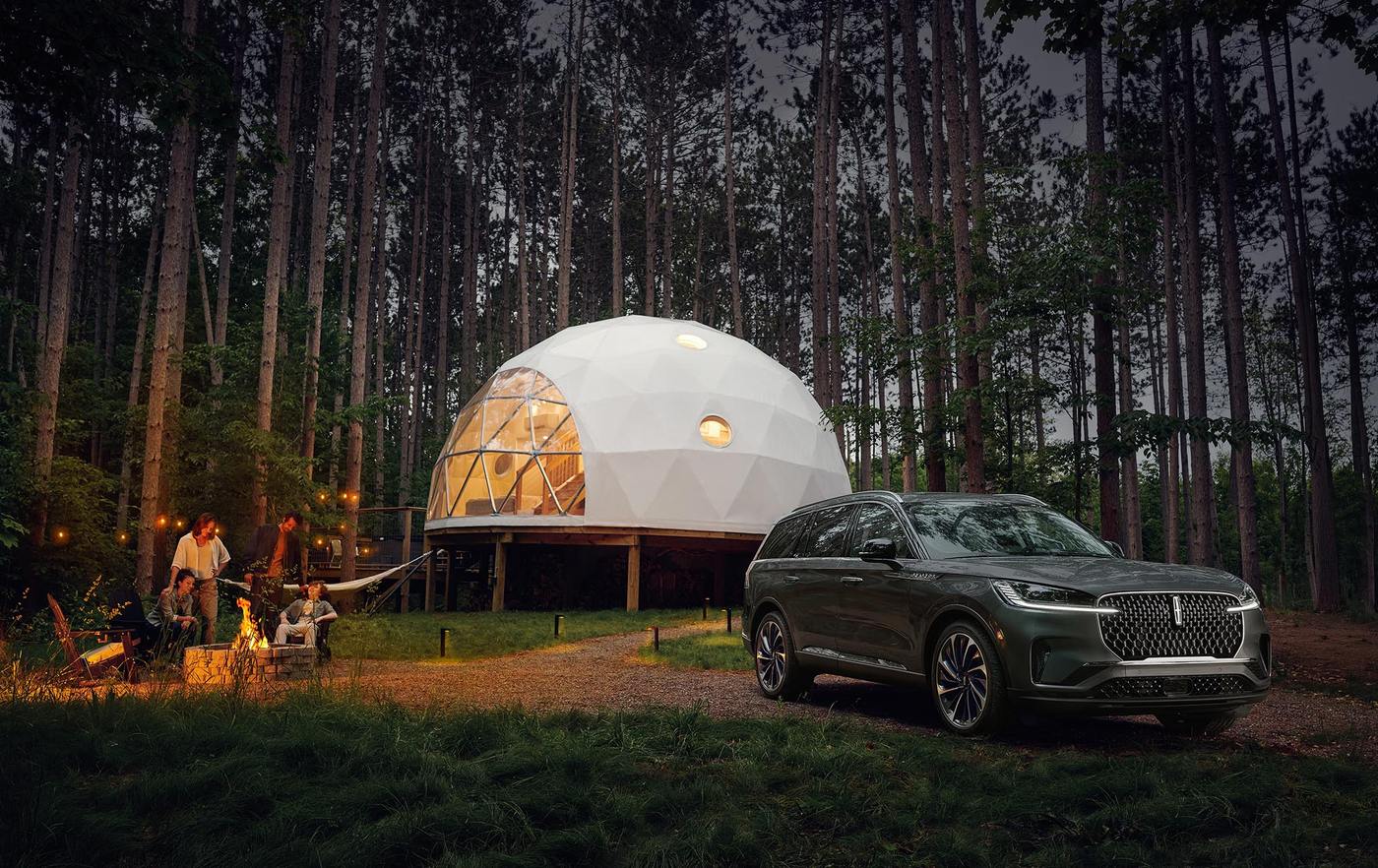 Lincoln Aviator parked at a forest campsite beside a lit dome tent