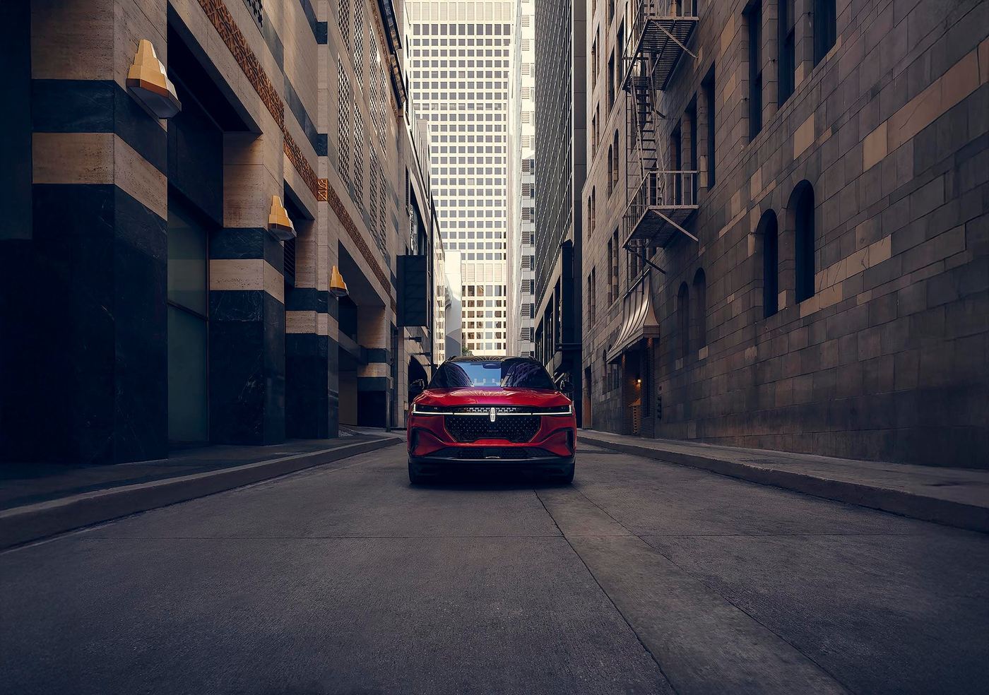 Red Lincoln Nautilus driving down a narrow downtown street between tall buildings