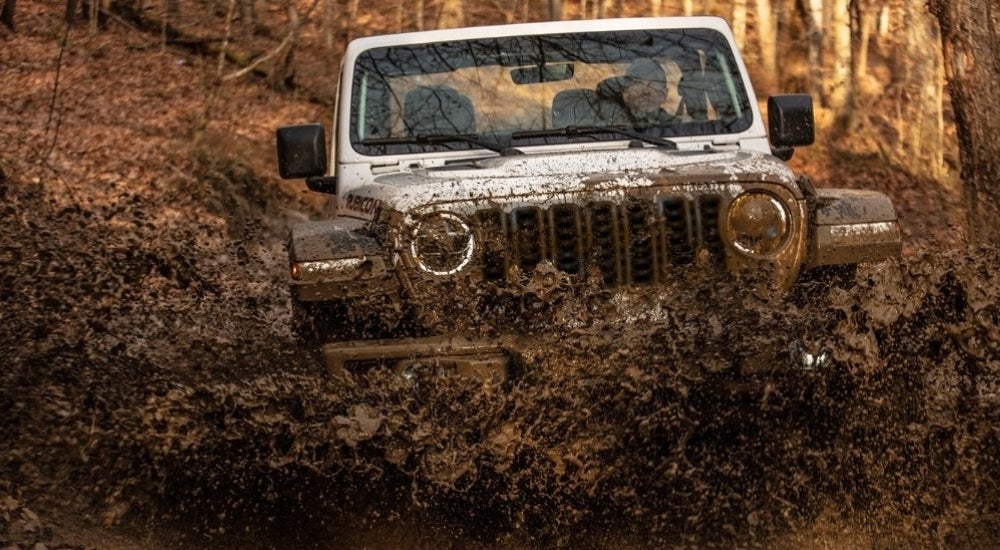 A silver 2024 Jeep Wrangler Rubicon for sale kicking up mud.