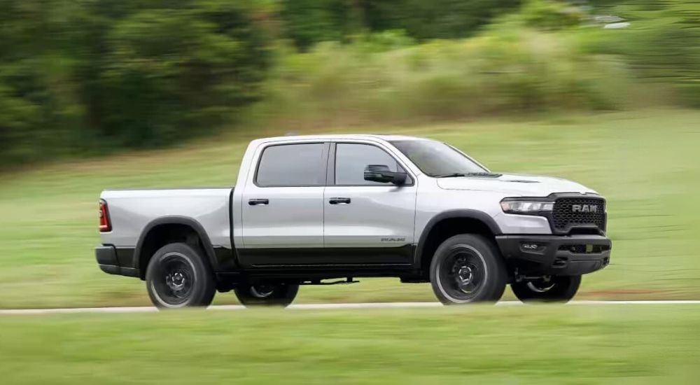 A silver 2025 Ram 1500 is driving on a grass-lined road.