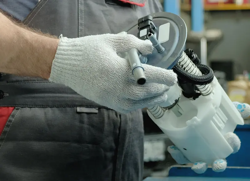 Mechanic in protective gloves assembling a car's fuel pump.