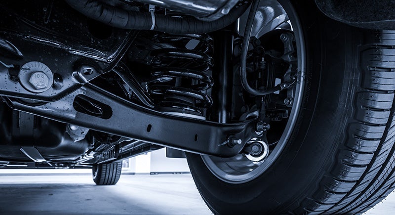 Underside view of a car with visible suspension components, including a tire, coil spring, and brake caliper.