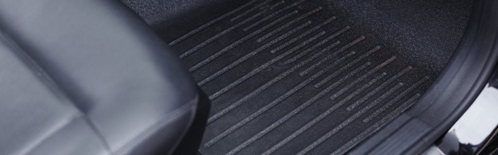 Close-up of a dark grey, ridged, rubber car floor mat and the edge of a black leather car seat.