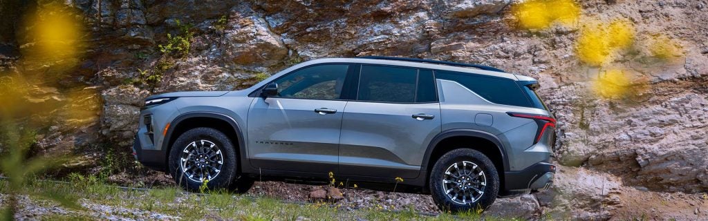Silver Chevrolet Traverse SUV parked beside a rocky cliff outdoors.