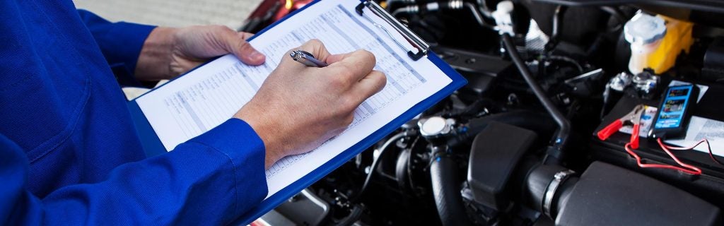 Mechanic filling out a checklist over a car engine.