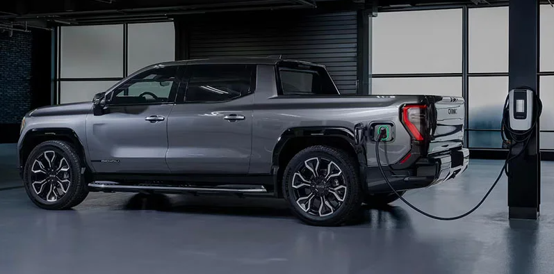 A silver 2025 GMC Sierra EV plugged in and charging in a garage.