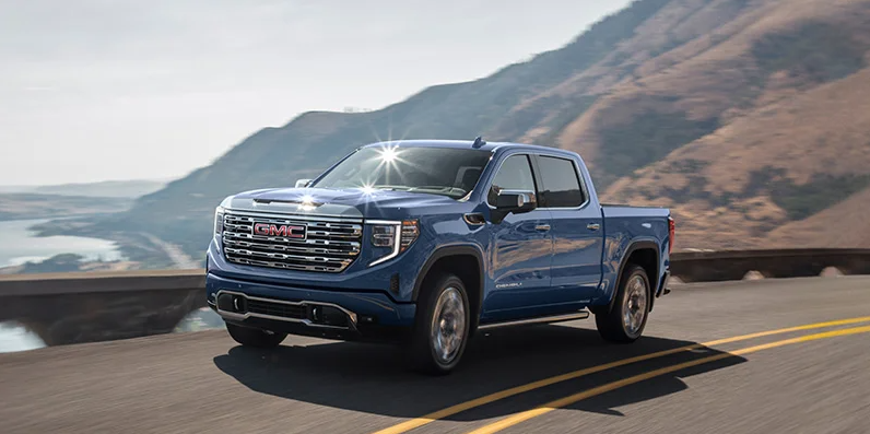 A blue 2025 GMC Sierra 1500 driving down a road with a beach in the backround.