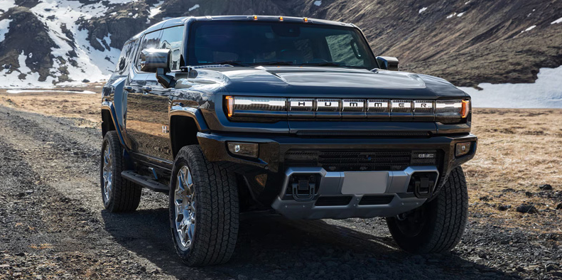 A black 2026 GMC Hummer EV driving down a dirt road.