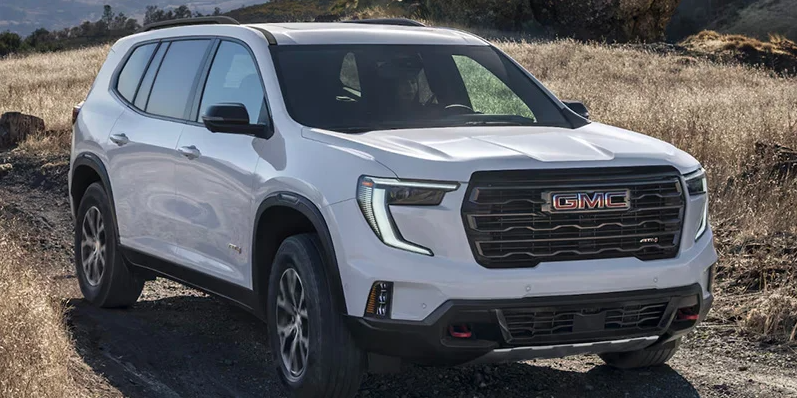 A white GMC Acadia driving down a dirt road.