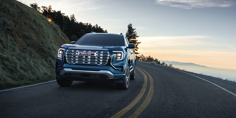 A blue 2026 GMC Acadia driving down the road.