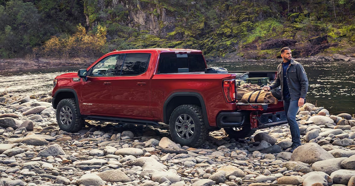 A man packing camping supplies into the bed of a red GMC Sierra 1500