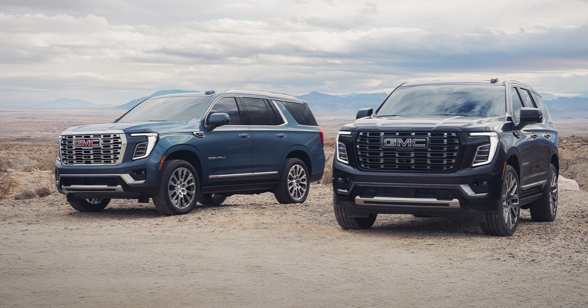 A blue GMC Yukon and a black GMC Yukon parked off-road by each other