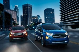 Red and Blue 2021 Ford EcoSport driving down a road with skyscrapers in the background.