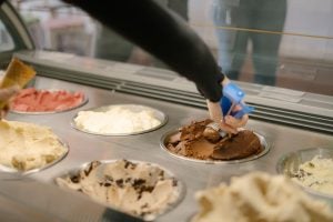 Close up of person scooping ice cream from an array of flavours.