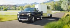 Black 2021 Chevrolet Silverado 2500 HD towing a trailer while driving on a country road.