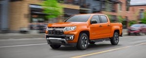 Orange Chevrolet Colorado driving down a town road.