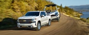 White Chevrolet Silverado 1500 towing a speed boat on a cliff road.