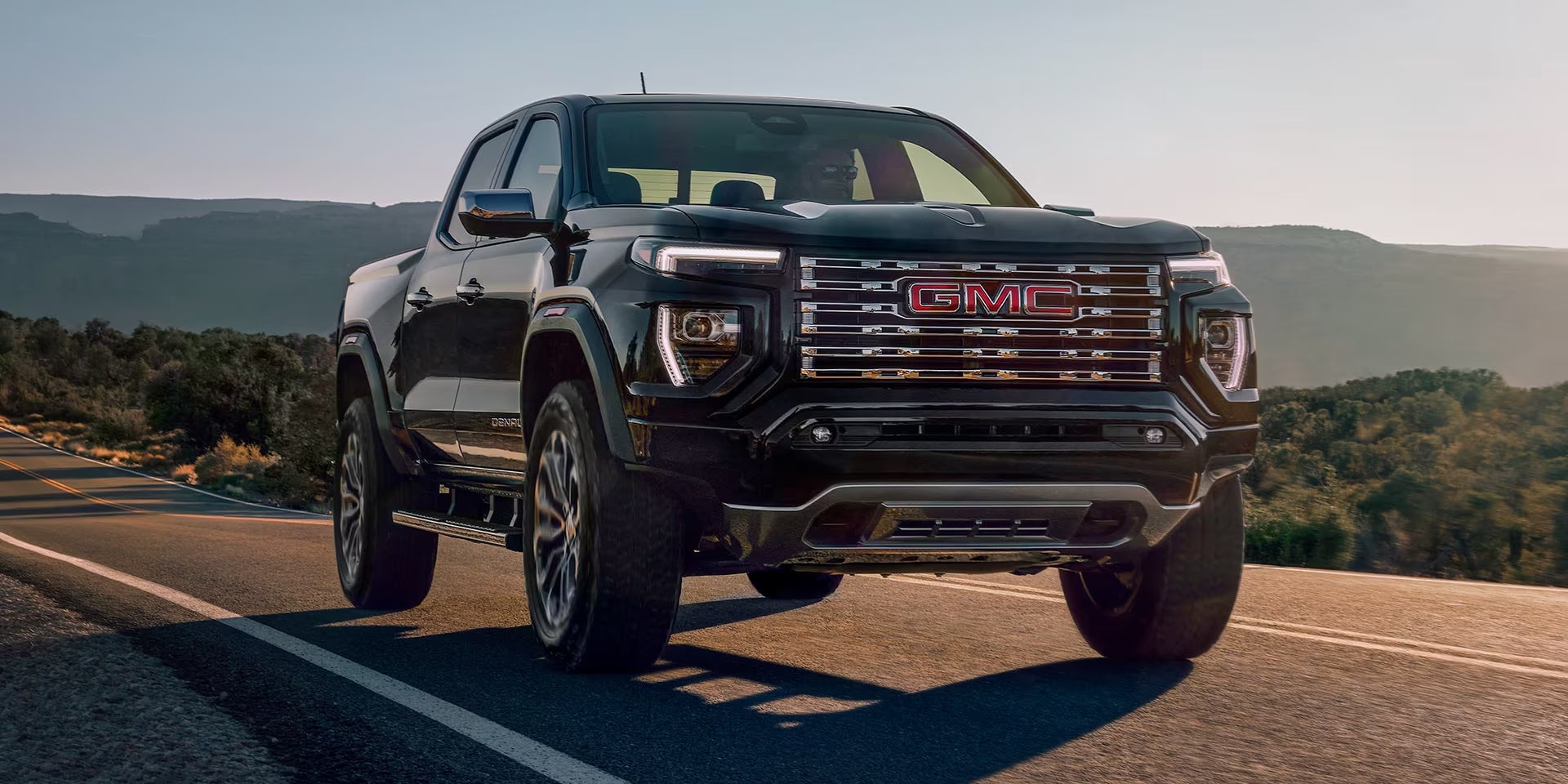 Black 2025 GMC Canyon truck driving on a road by a mountain range