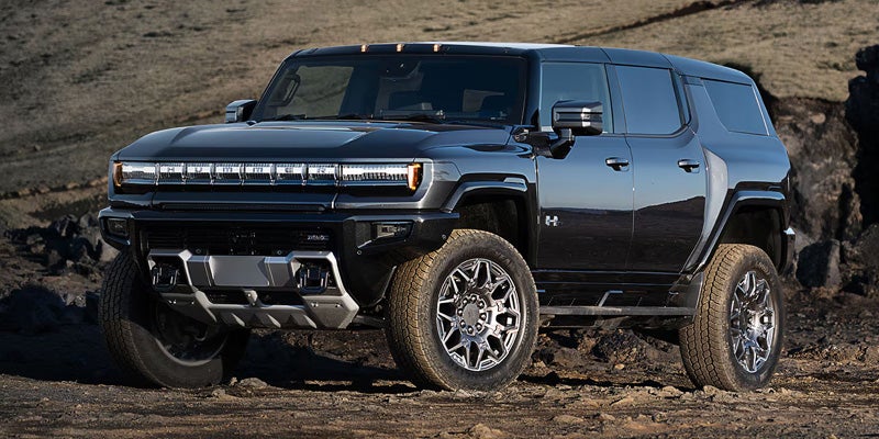 Black electric Hummer SUV parked on rocky terrain, shown from the front side.