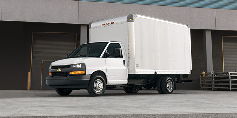 White Chevrolet box truck parked outside a commercial warehouse building.
