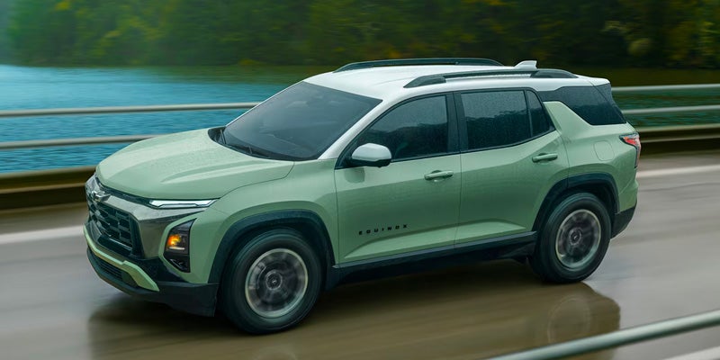 High-angle view of a sage green Chevrolet Equinox with a white roof driving across a bridge next to a body of water.