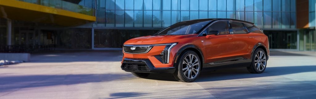 Orange Cadillac electric SUV parked in front of a modern glass building.