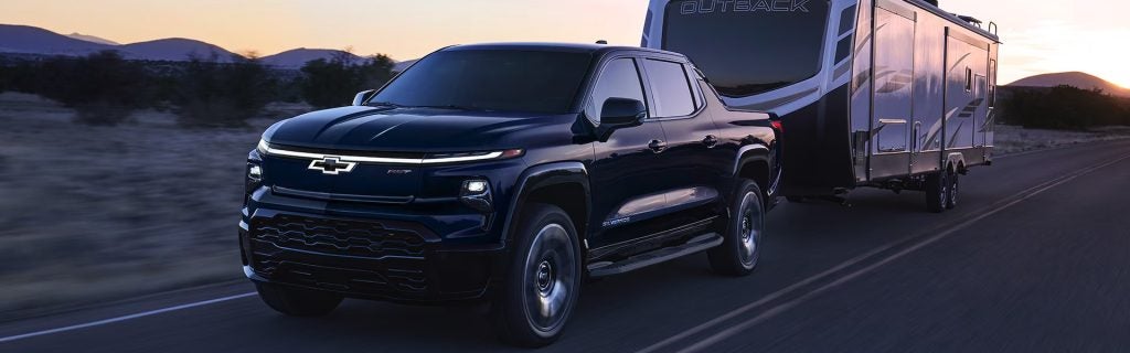 Chevrolet Silverado EV towing a camper trailer on a scenic road.