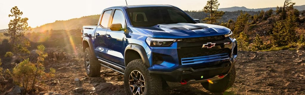 Blue Chevrolet pickup truck driving off-road on a rocky trail at sunset.