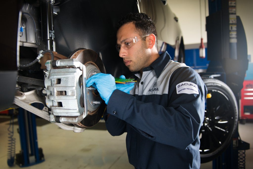 Technician inspecting a vehicle brake assembly while wearing safety glasses and gloves in a service bay.
