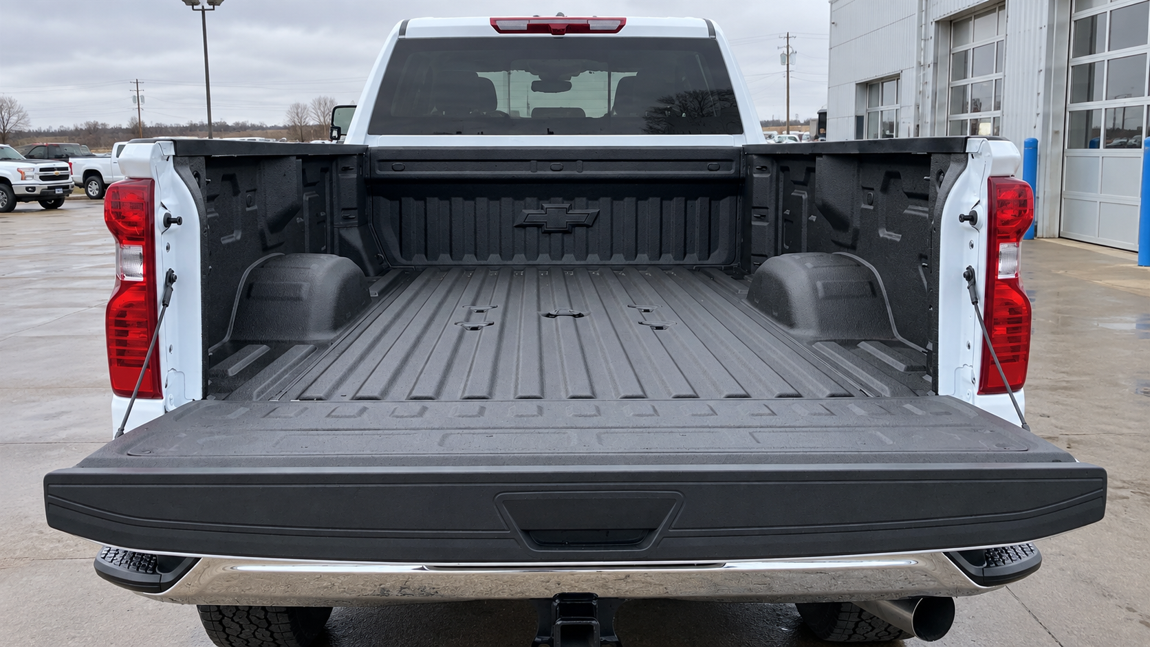 Open bed of a Chevrolet Silverado 3500 HD in Summit White seen from behind the lowered tailgate, showing the Durabed floor, tie-down caps and the stamped bowtie