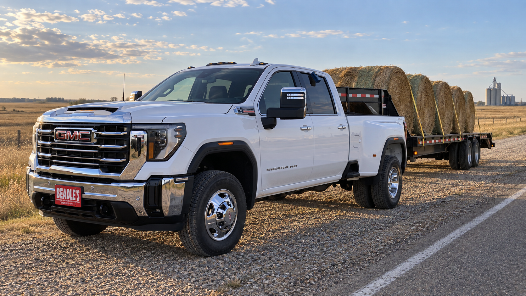 2026 GMC Sierra 3500 HD SLT dually in Summit White with a gooseneck hay trailer on a two-lane shoulder near Mobridge, South Dakota