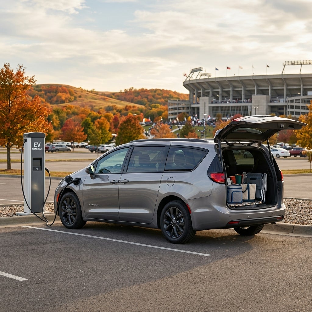Silver hybrid minivan plugged into an EV charging station outside a sports stadium with autumn trees in the background. (Representative image for illustration purposes only. Actual vehicle may vary based on trim and configuration.)