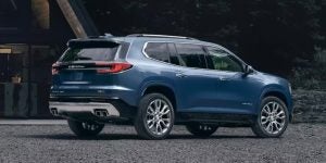 Side profile of a 2024 GMC Acadia parked outside of a home.