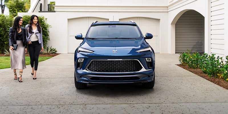 Blue 2024 Buick Encore GX parked in driveway with vehicle headlights and grill facing front and two women walking toward vehicle
