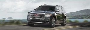 Black GMC Acadia driving down a hill road.