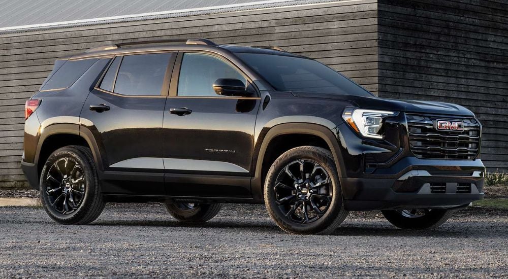 A black 2025 GMC Terrain Elevation parked outside a barn.
