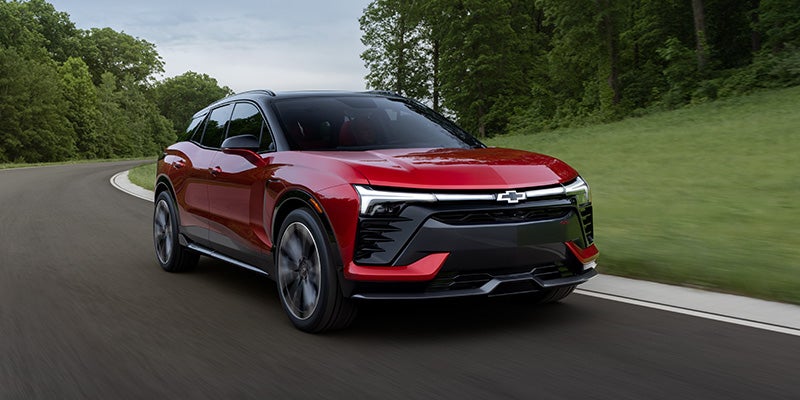2026 red Chevrolet Blazer EV driving on a curved road with green trees in the background