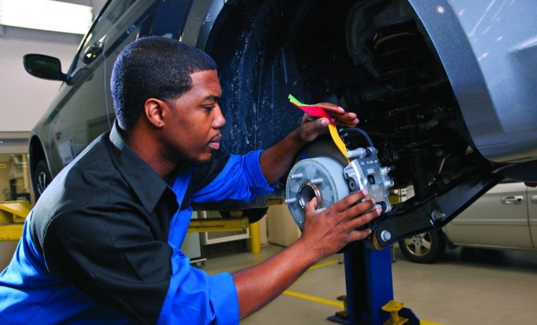 Auto technician inspecting and working on a vehicle brake assembly inside a service garage