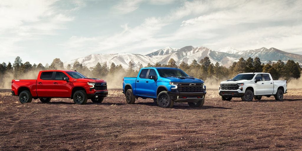 A lineup of three Chevy Silverado pickup trucks parked in a mountainous landscape.