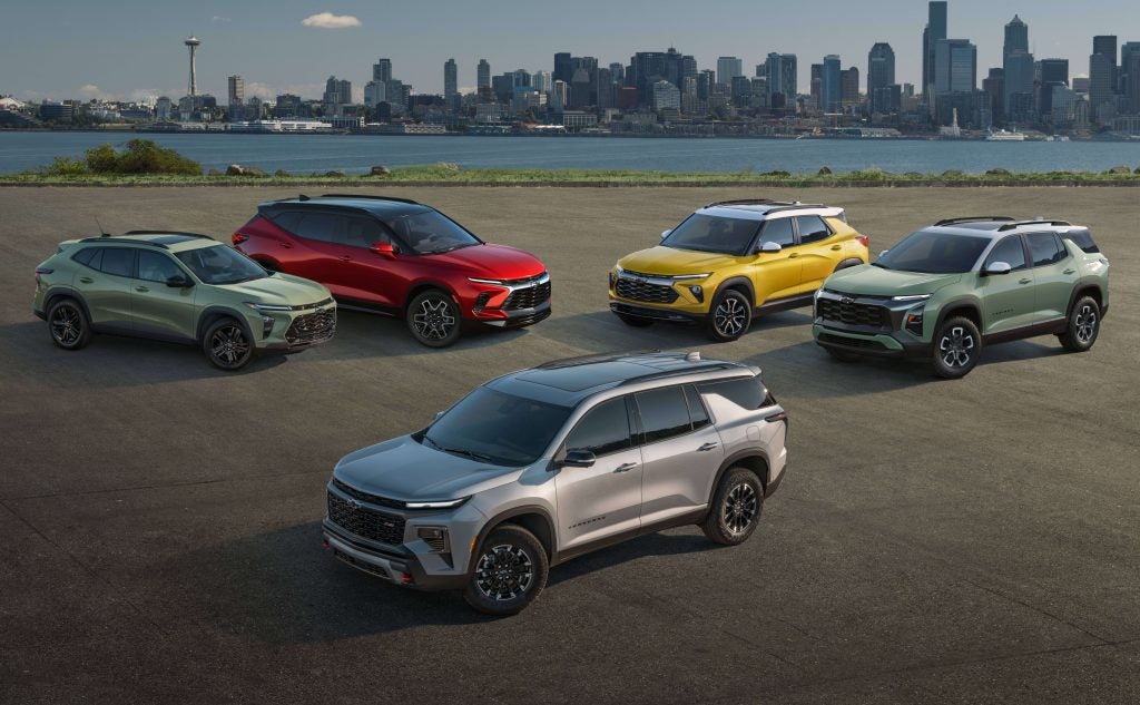 A lineup of five colorful Chevy SUVs parked with a city skyline in the background.