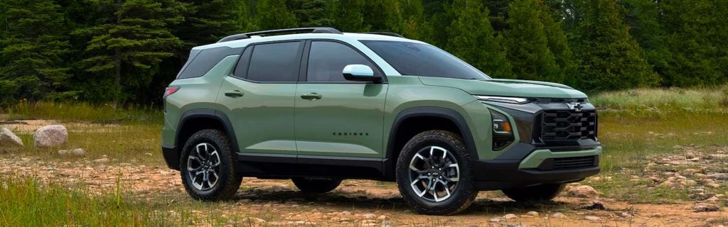 Cacti Green Chevrolet Equinox parked in a grassy field with a pine forest background.
