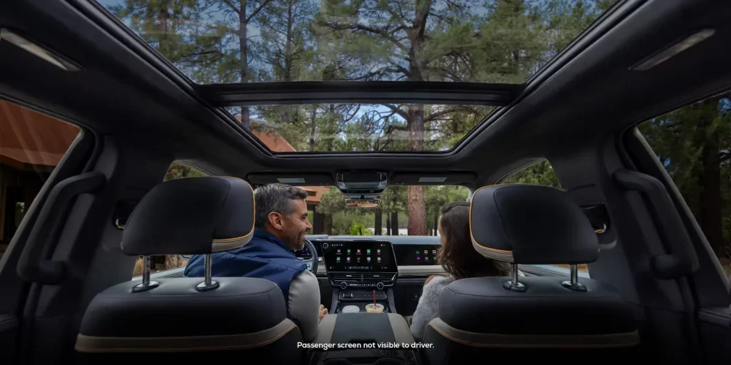 A man in the driver seat and a woman in the passenger seat of a 2027 Chevrolet Silverado with the photo from the back seats panning at the expansive sunroof.