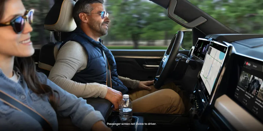 A photo from the perspective of the passenger showing a woman in the passenger seat and a man in the diver seat smiling. The woman is looking at YouTube on the screen in front of her.