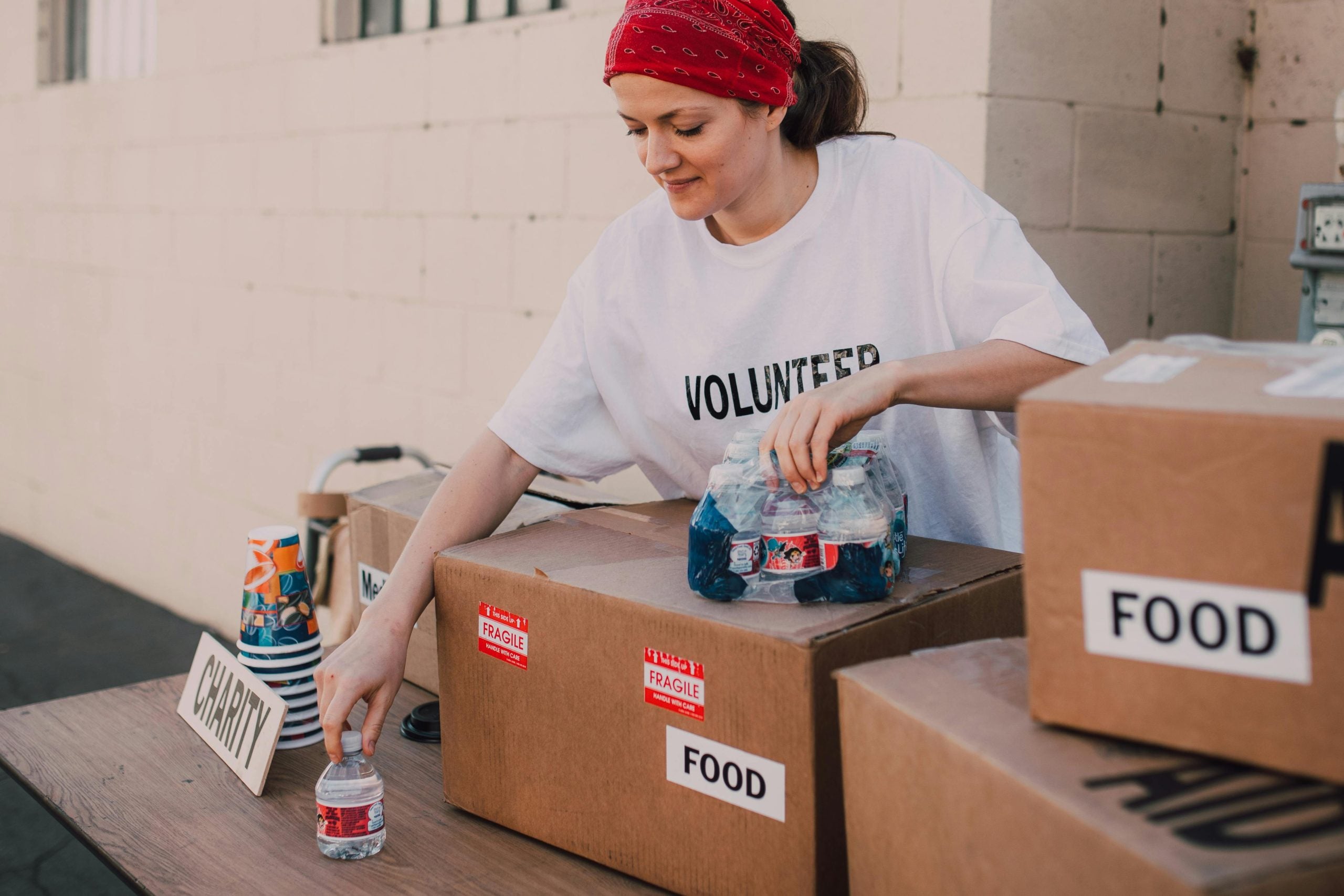 A Woman Wearing Volunteer Shirt Displaying Bottled Water on Table