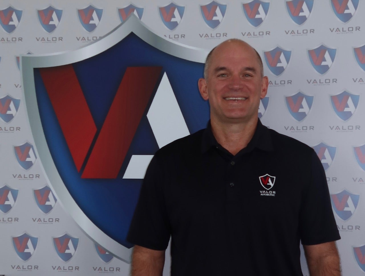 Smiling man in a black polo shirt standing in front of a Valor Automotive branded background.