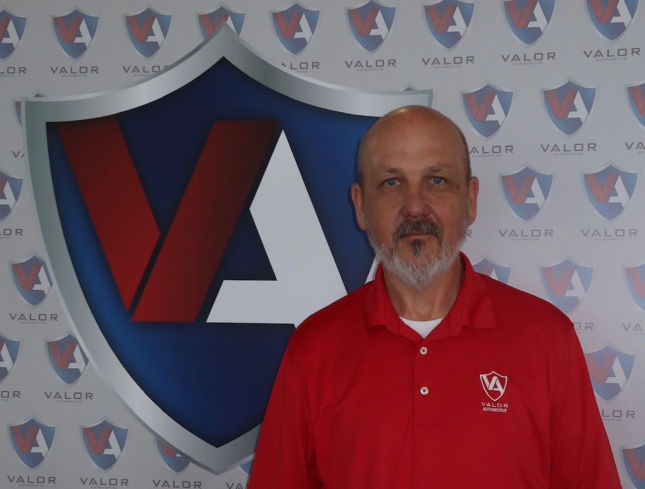 Man in a red polo shirt standing in front of a Valor Automotive logo backdrop.