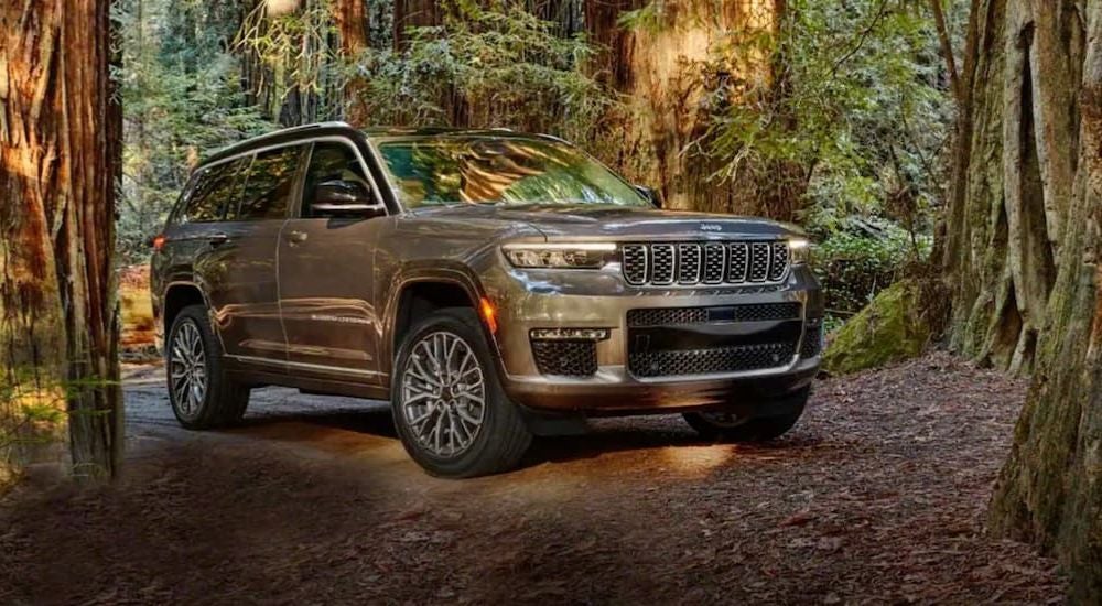 A tan 2021 Jeep Grand Cherokee L driving off-road past large trees.