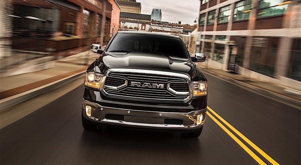 Front of a black used 2015 Ram 1500 for sale driving through a city.