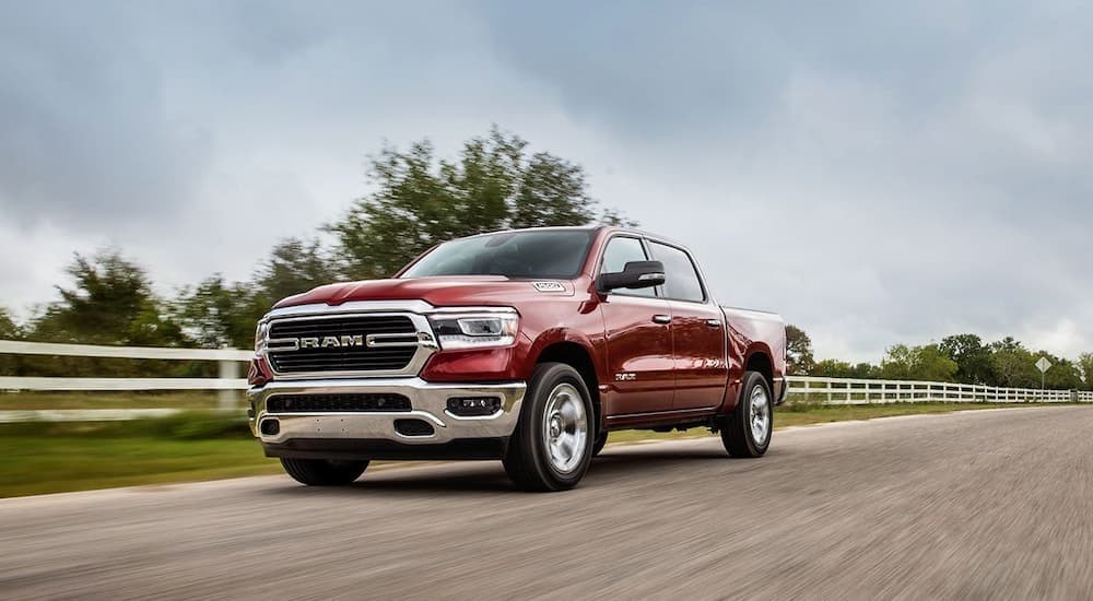 A red 2020 Ram 1500 for sale driving near a white fence.